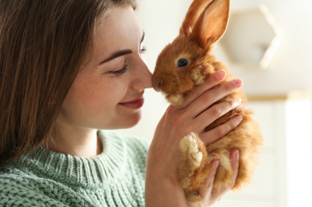  Foto de uma mulher branca e ruiva segurando um coelho marrom claro para ilustrar o movimento cruelty free.